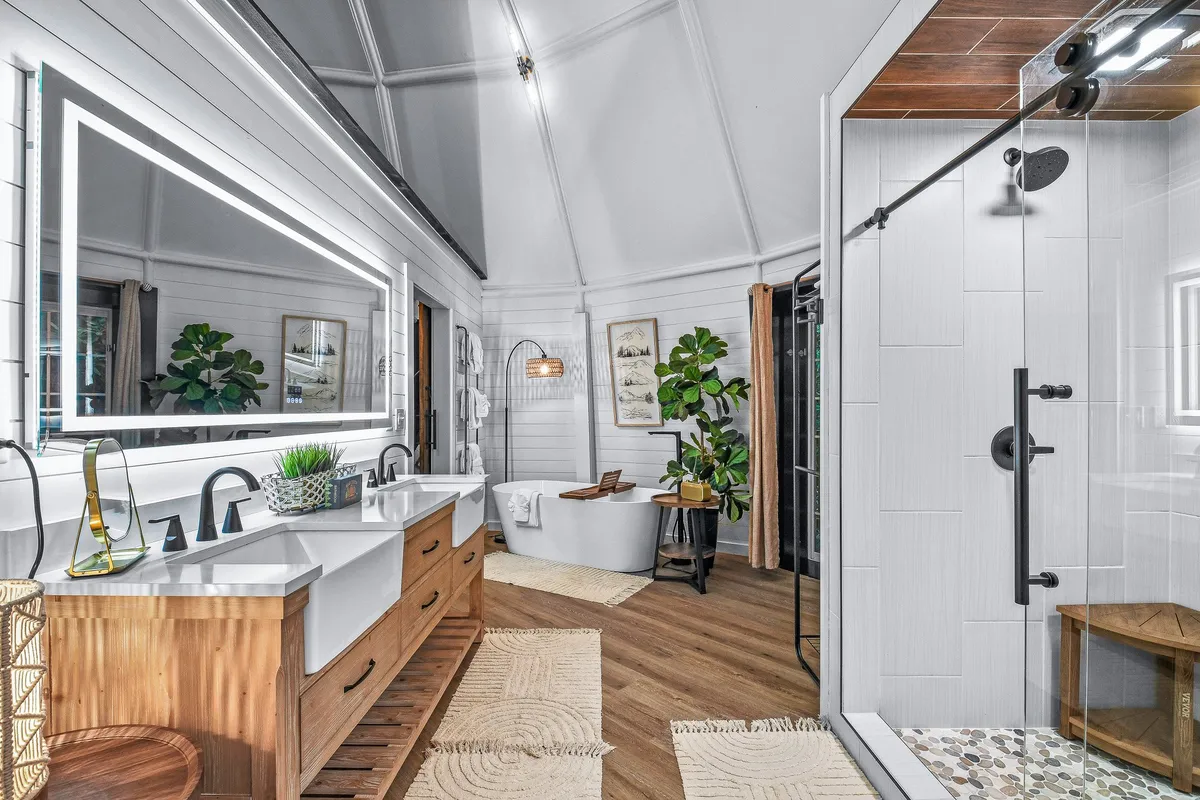 A luxurious, spa-like master bathroom featuring a double vanity with modern fixtures, a large mirror with soft LED lighting, a sleek freestanding bathtub, and a spacious glass-enclosed shower area. The space feels bright, calming, and inviting—perfect for both morning routines and evening relaxation.
