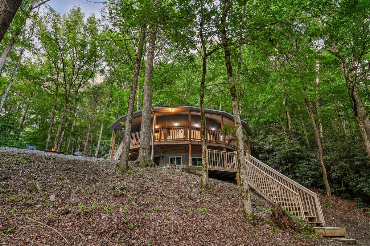 A tranquil view of a circular wooden deck set amidst tall trees, highlighting the seamless integration with nature. The area is spacious, ideal for relaxing outdoors, with subtle hints of nearby trails and the woodland surroundings that beckon exploration.