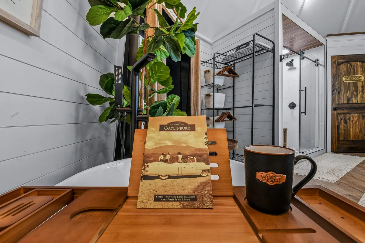 A cozy interior scene shows a wooden tray with a coffee mug and a Gatlinburg travel brochure, placed beside a lush green plant. In the background, a clothes rack adds a lived-in feel. The image suggests planning and savoring local adventures in comfort.