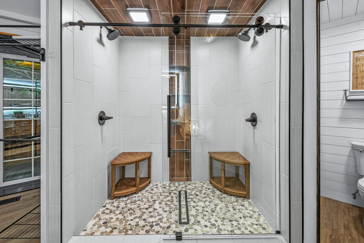 A tranquil shower space with a spacious walk-in design, natural wood accents, and pebble stone flooring. The environment is minimalist yet inviting, exuding a spa-like ambiance ideal for invigorating showers and peaceful unwinding.